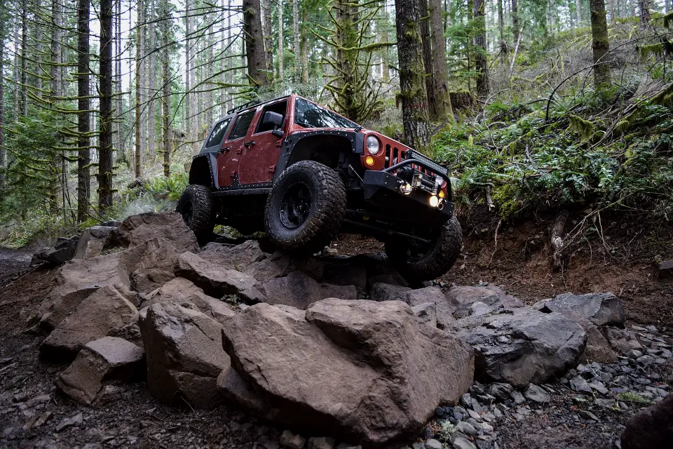 A lifted 4x4 climbing over rocks on a forested trail.